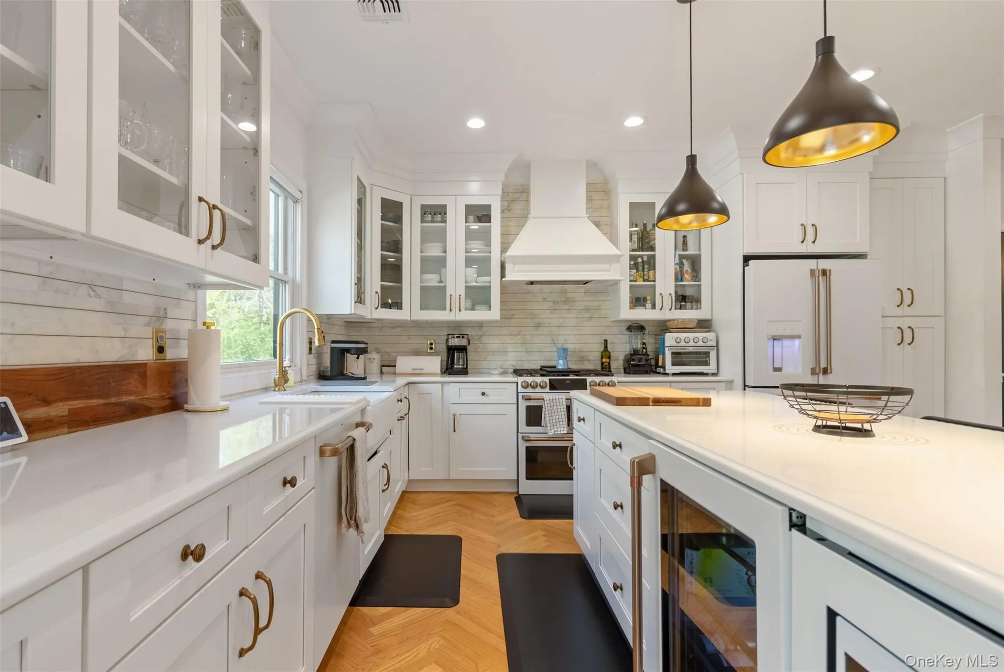 Kitchen with custom exhaust hood, white cabinets, range with two ovens, a sink, and white fridge with ice dispenser Kitchen with custom exhaust hood, white cabinets, range with two ovens, a sink, and white fridge with ice dispenser