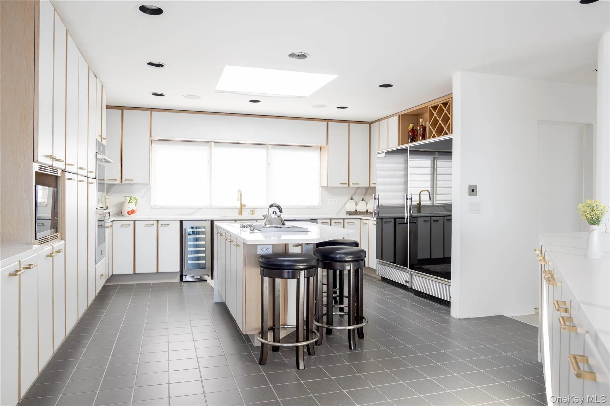 Kitchen featuring light countertops, a skylight, an island with sink, and wine cooler Kitchen featuring light countertops, a skylight, an island with sink, and wine cooler