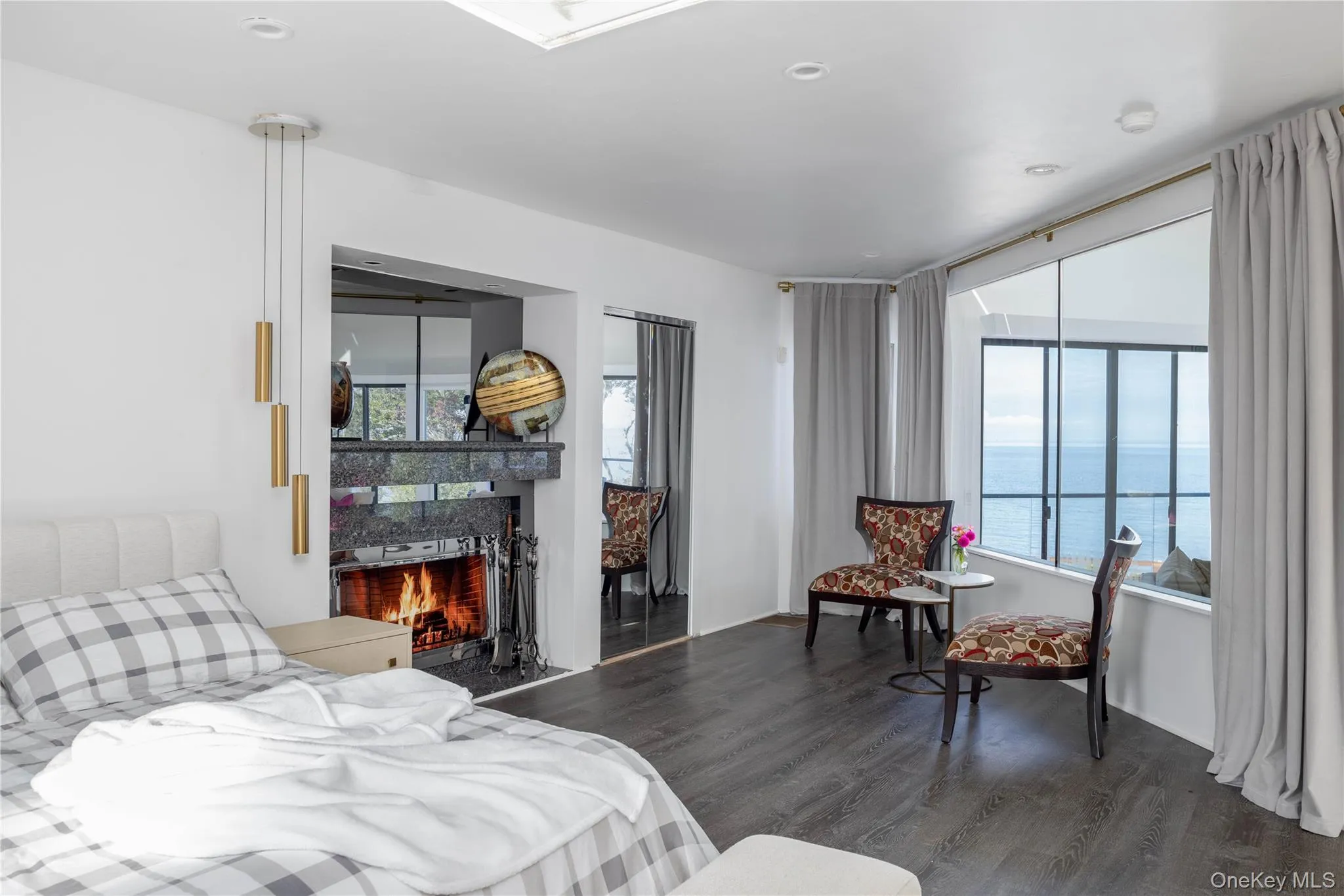 Bedroom featuring a water view, a warm lit fireplace, and wood finished floors Bedroom featuring a water view, a warm lit fireplace, and wood finished floors