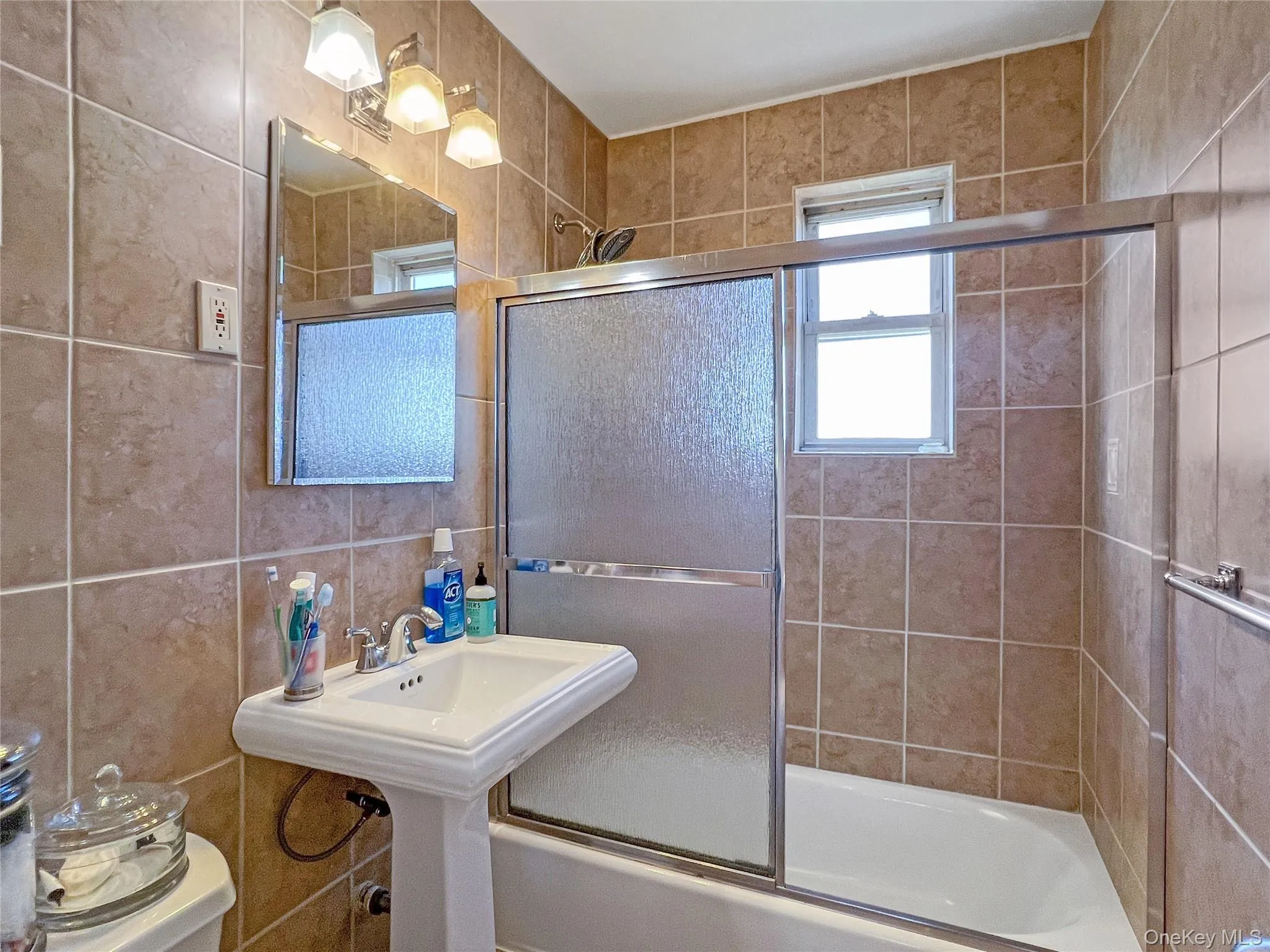 Full bathroom featuring tile walls, toilet, and bath / shower combo with glass door Full bathroom featuring tile walls, toilet, and bath / shower combo with glass door
