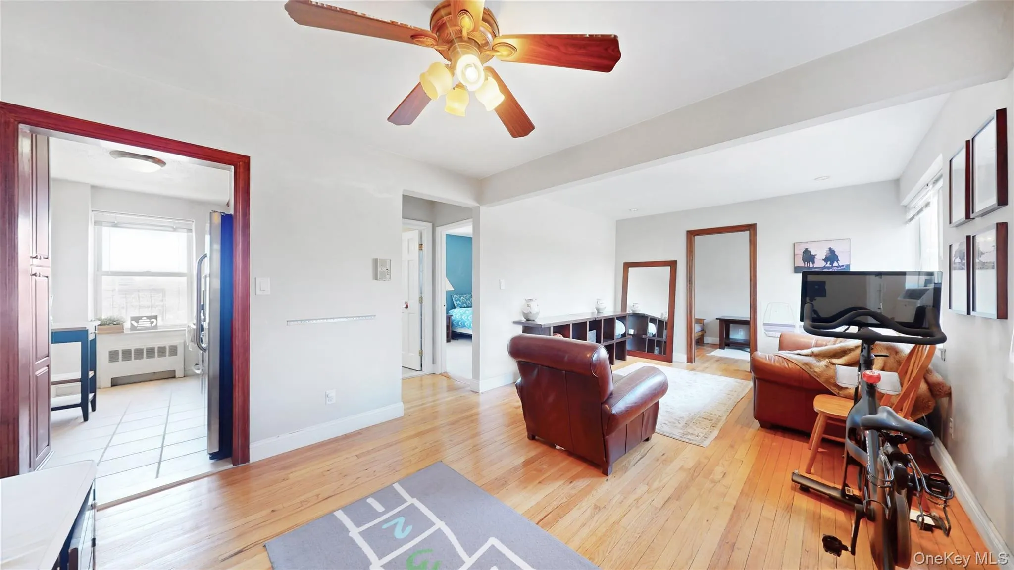 Living room featuring light wood finished floors, baseboards, ceiling fan, and radiator heating unit Living room featuring light wood finished floors, baseboards, ceiling fan, and radiator heating unit