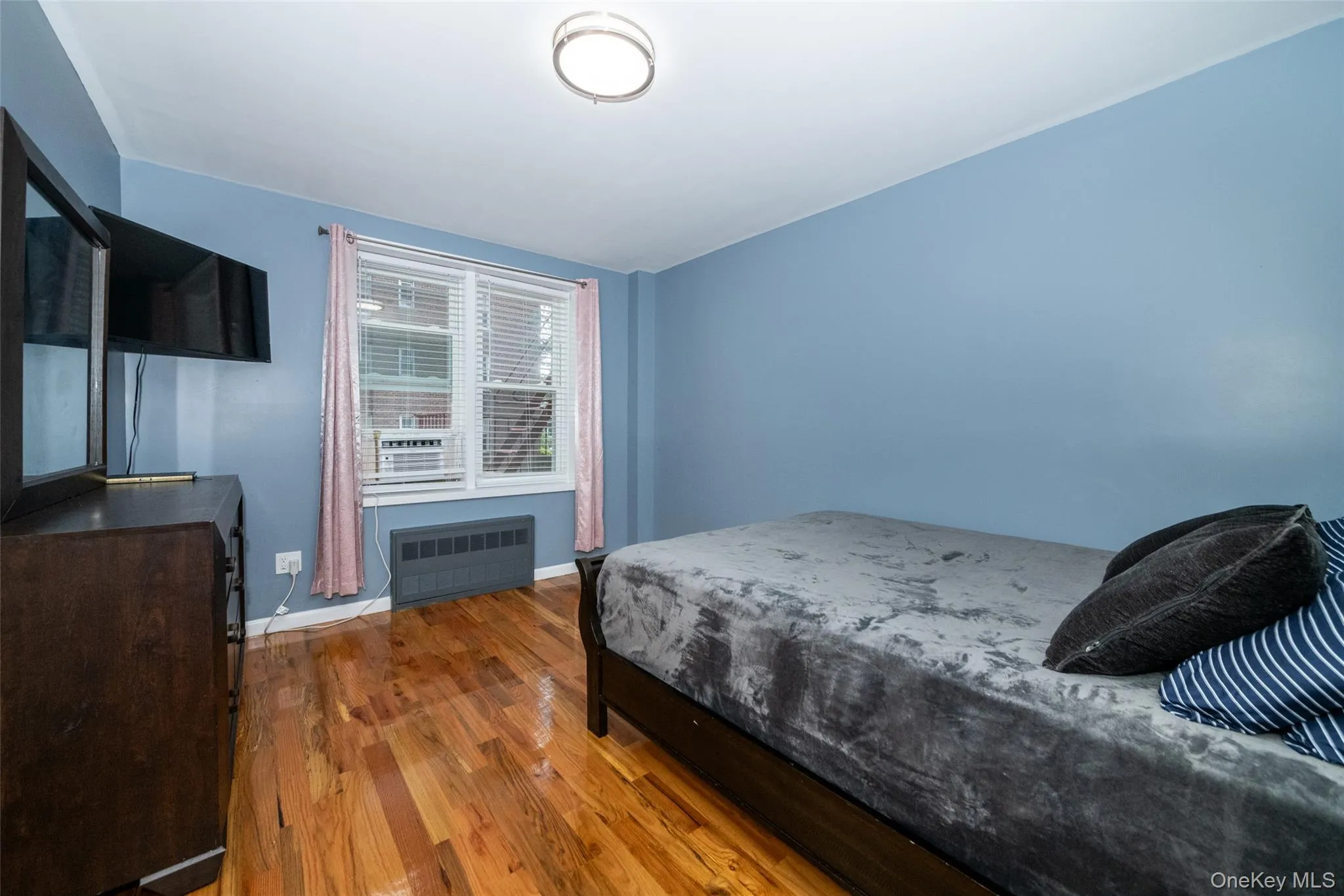 Bedroom featuring radiator heating unit, wood finished floors, and baseboards Bedroom featuring radiator heating unit, wood finished floors, and baseboards