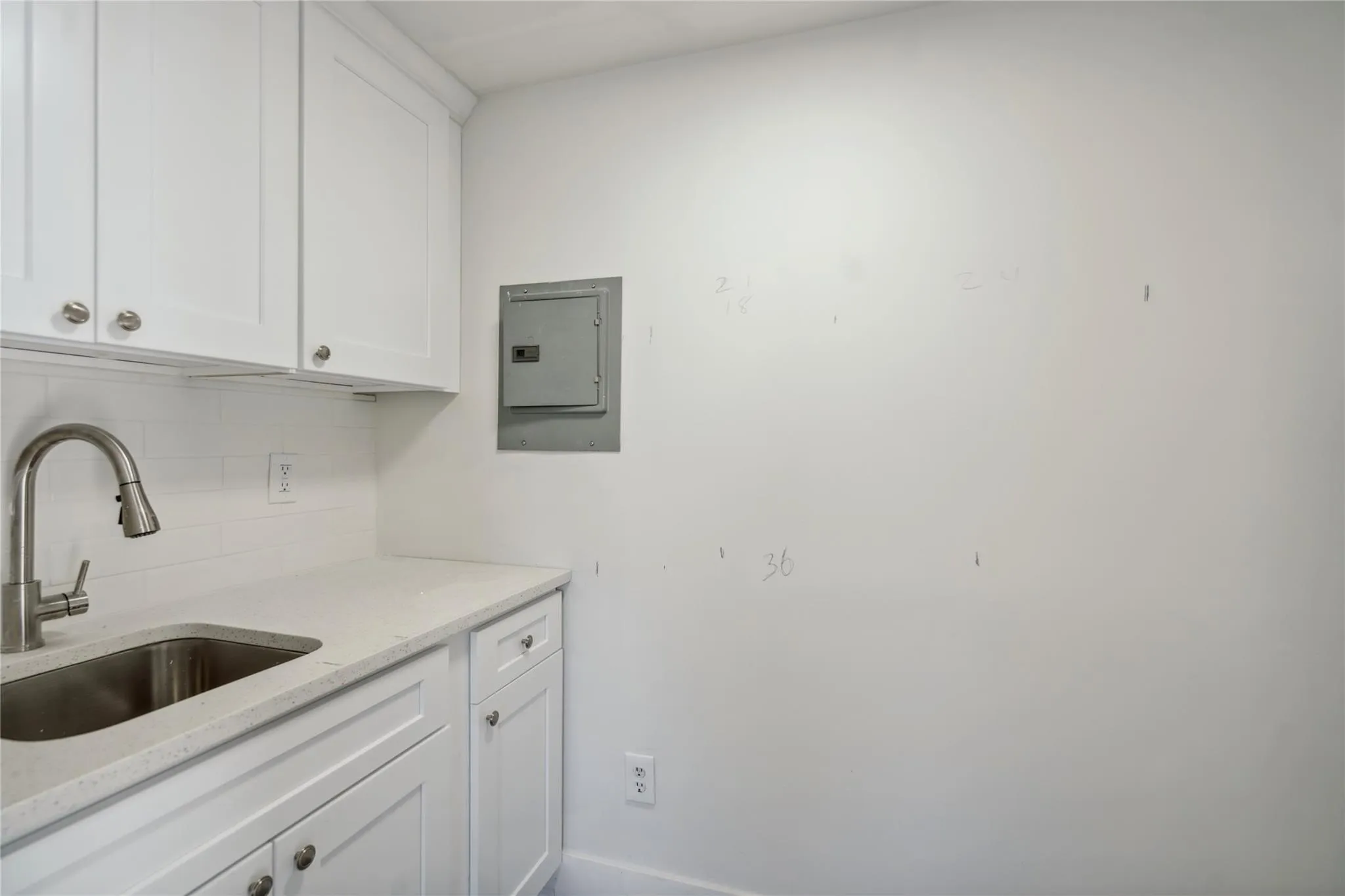 Kitchen featuring backsplash, white cabinetry, a sink, and electric panel Kitchen featuring backsplash, white cabinetry, a sink, and electric panel