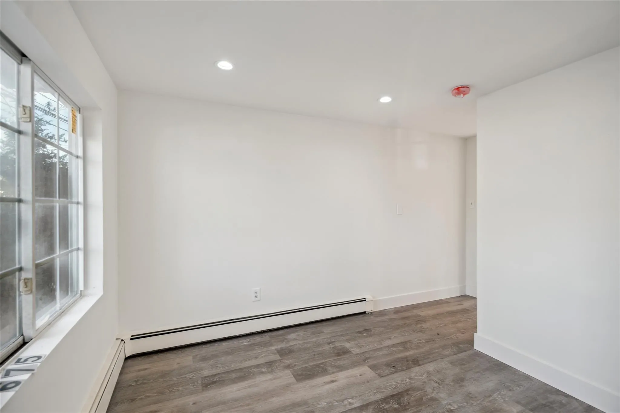 Unfurnished room with baseboards, wood finished floors, a baseboard radiator, and recessed lighting Unfurnished room with baseboards, wood finished floors, a baseboard radiator, and recessed lighting