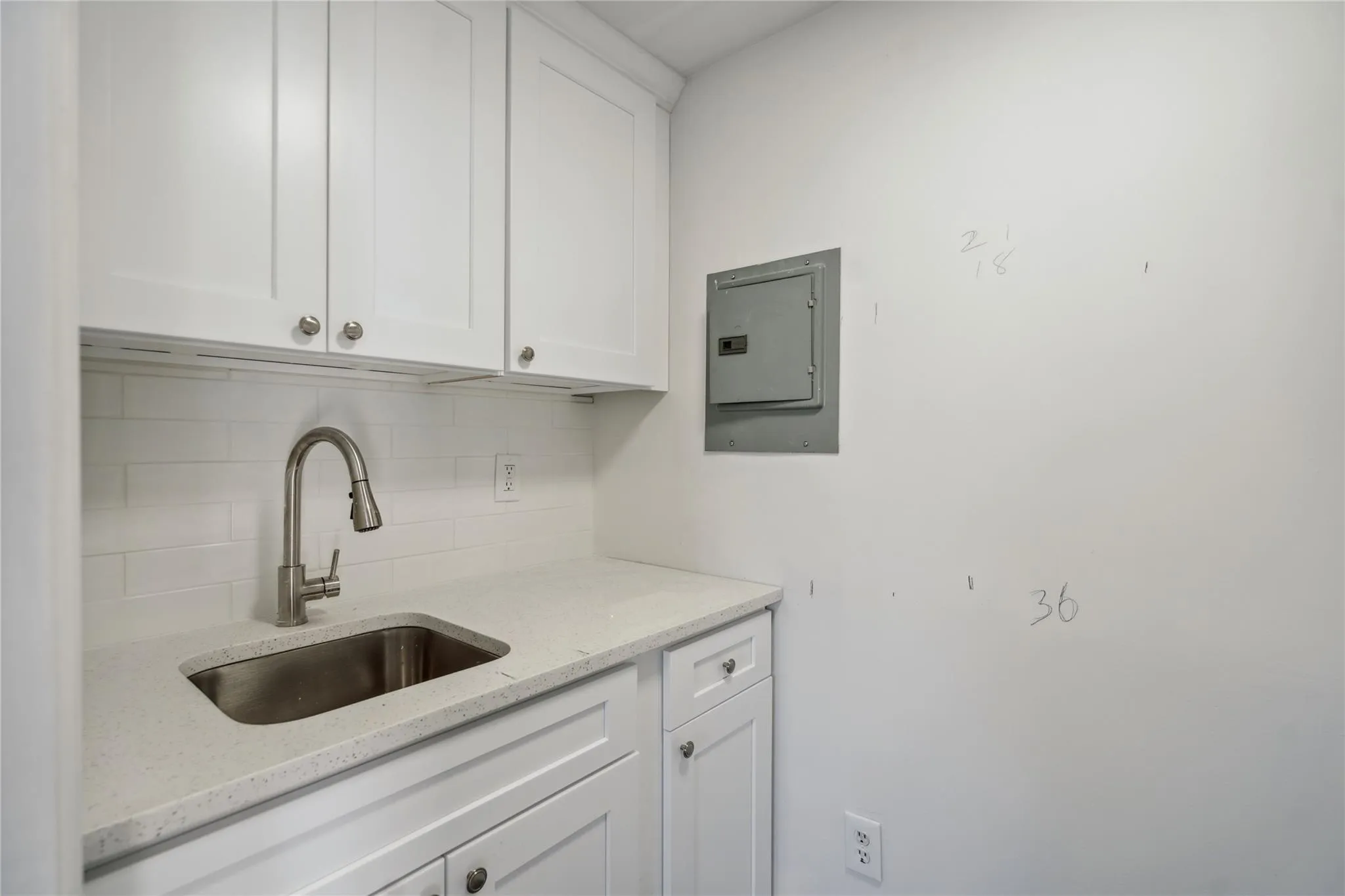 Kitchen featuring a sink, electric panel, tasteful backsplash, light stone counters, and white cabinetry Kitchen featuring a sink, electric panel, tasteful backsplash, light stone counters, and white cabinetry