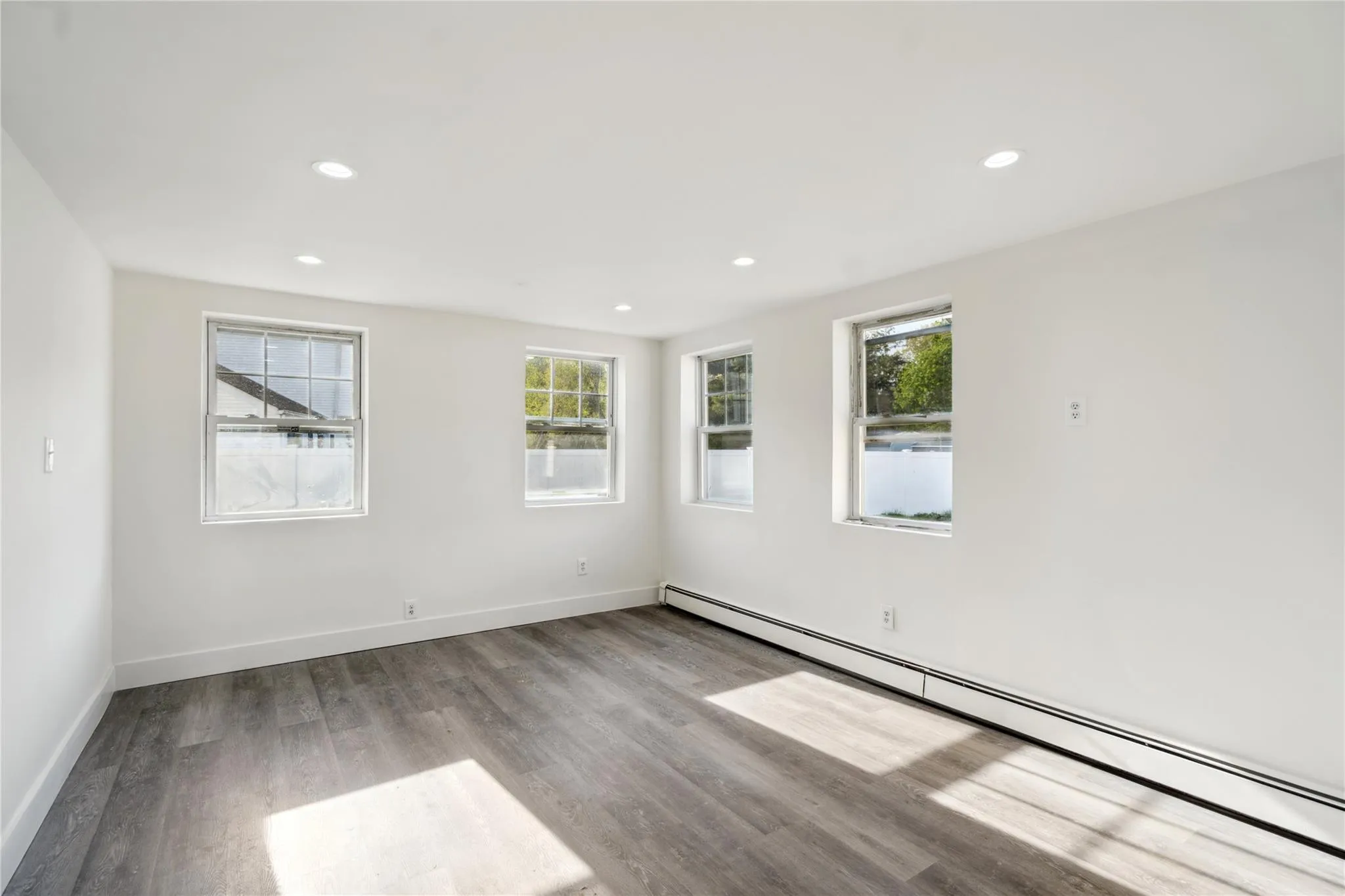 Empty room with a healthy amount of sunlight, wood finished floors, baseboards, and a baseboard heating unit Empty room with a healthy amount of sunlight, wood finished floors, baseboards, and a baseboard heating unit