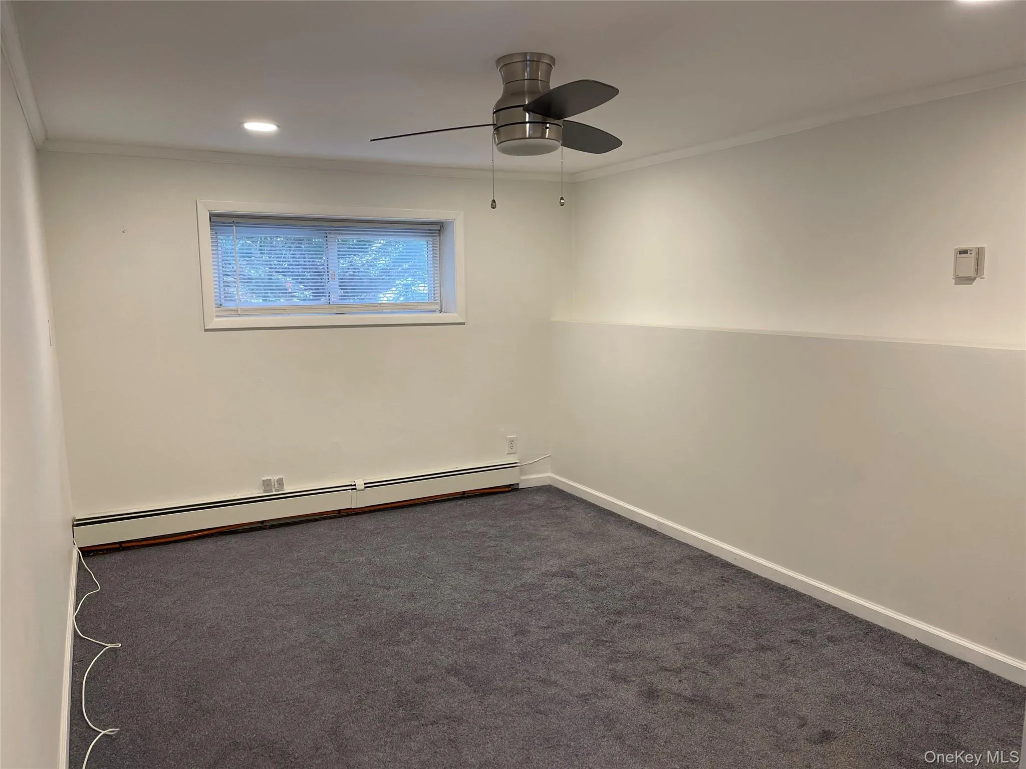 Empty room featuring recessed lighting, baseboard heating, ornamental molding, dark colored carpet, and a ceiling fan Empty room featuring recessed lighting, baseboard heating, ornamental molding, dark colored carpet, and a ceiling fan