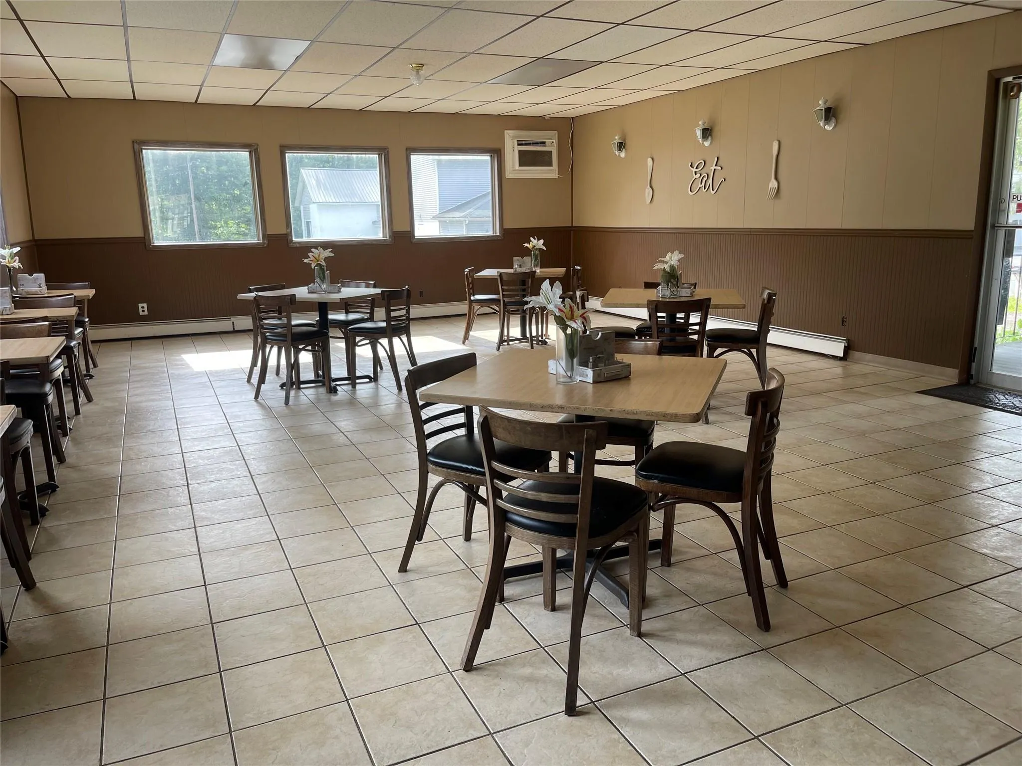 Dining room featuring healthy amount of natural light, a baseboard radiator, light tile patterned floors, a drop ceiling, and wainscoting Dining room featuring healthy amount of natural light, a baseboard radiator, light tile patterned floors, a drop ceiling, and wainscoting