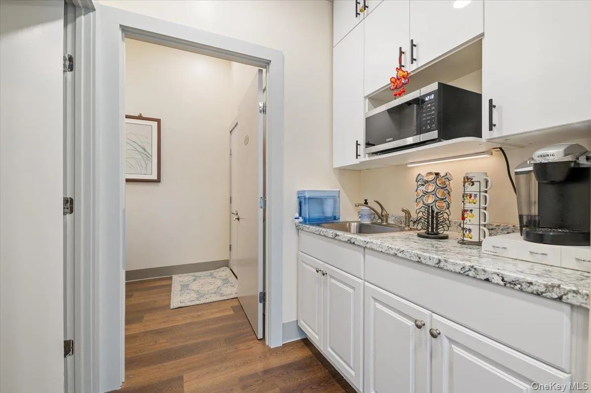 Kitchen featuring stainless steel microwave, a sink, white cabinetry, and dark wood finished floors Kitchen featuring stainless steel microwave, a sink, white cabinetry, and dark wood finished floors