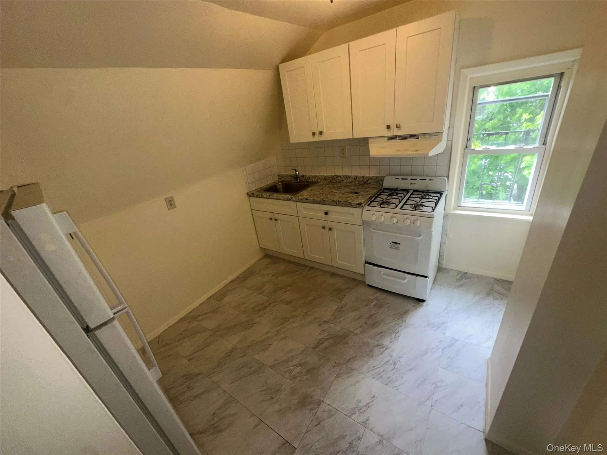 Kitchen featuring vaulted ceiling, under cabinet range hood, white range with gas stovetop, and white cabinets Kitchen featuring vaulted ceiling, under cabinet range hood, white range with gas stovetop, and white cabinets