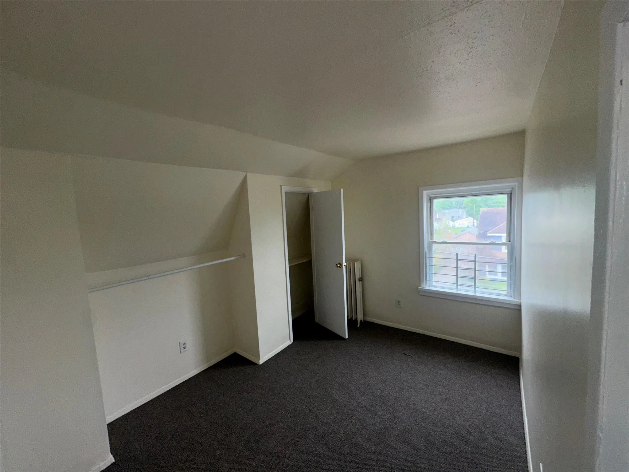 Additional living space with baseboards, dark carpet, radiator heating unit, and vaulted ceiling Additional living space with baseboards, dark carpet, radiator heating unit, and vaulted ceiling