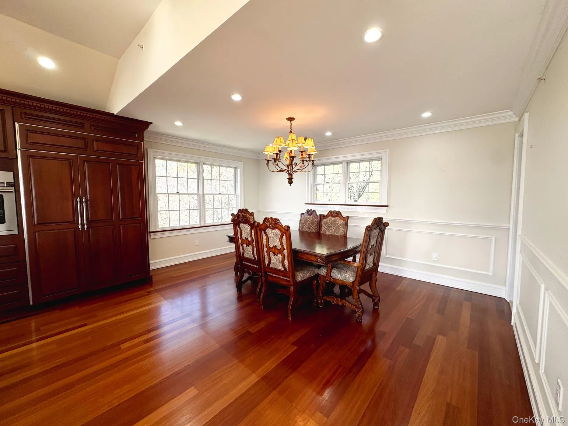 Dining area with dark wood-style flooring, ornamental molding, recessed lighting, a chandelier, and a wainscoted wall Dining area with dark wood-style flooring, ornamental molding, recessed lighting, a chandelier, and a wainscoted wall