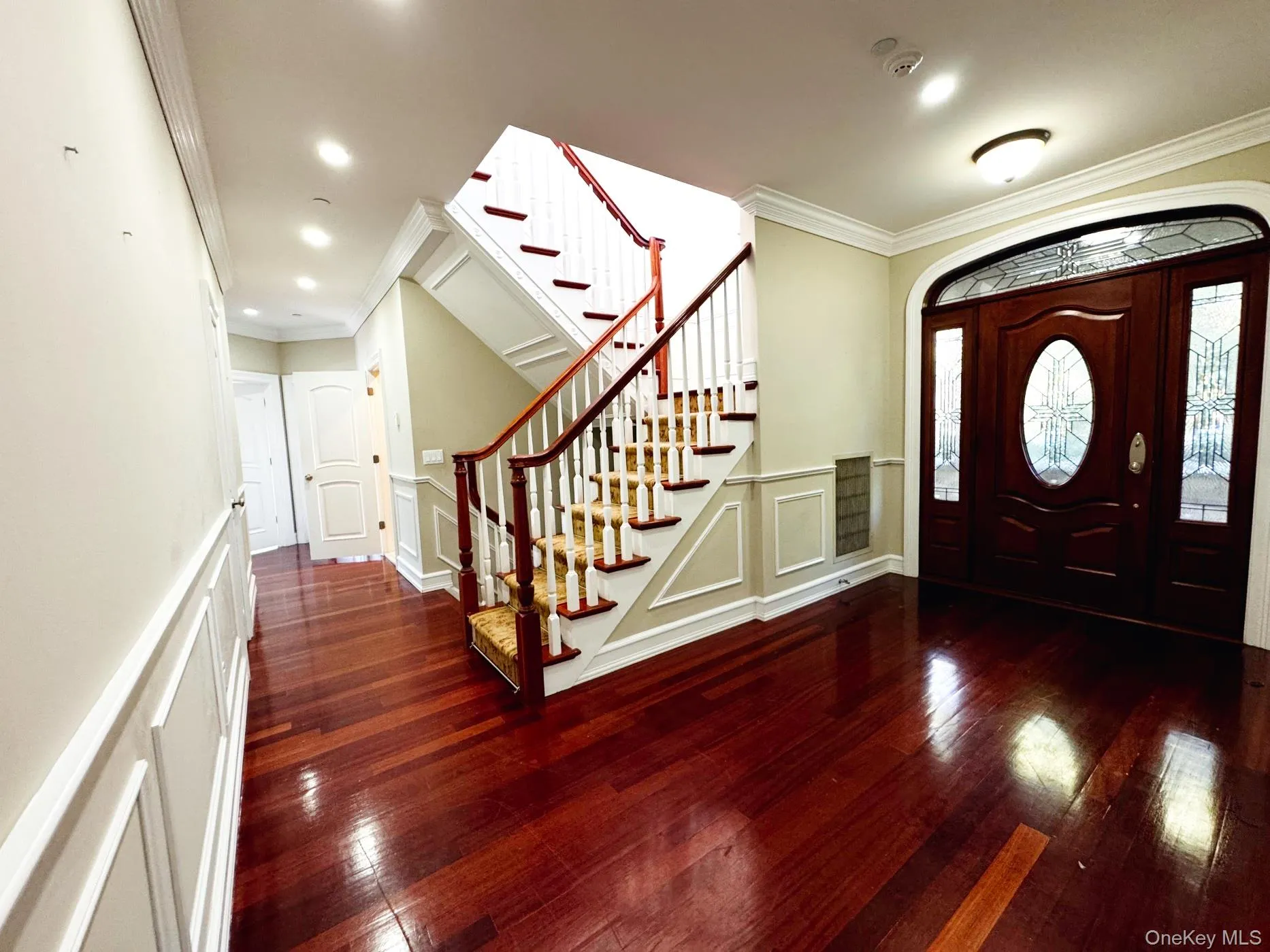 Foyer entrance featuring ornamental molding, stairway, dark wood finished floors, a decorative wall, and wainscoting Foyer entrance featuring ornamental molding, stairway, dark wood finished floors, a decorative wall, and wainscoting