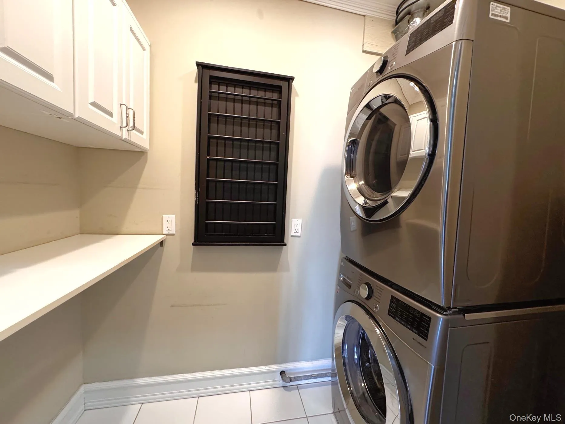 Washroom featuring light tile patterned floors, stacked washing machine and dryer, and cabinet space Washroom featuring light tile patterned floors, stacked washing machine and dryer, and cabinet space