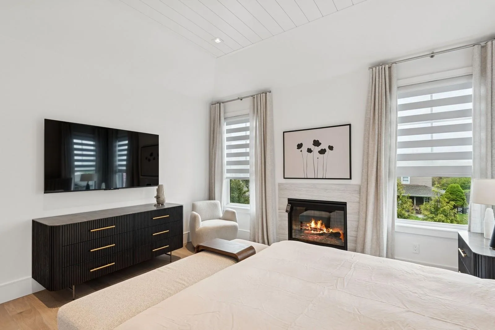 Bedroom featuring wood finished floors, multiple windows, a glass covered fireplace, and baseboards Bedroom featuring wood finished floors, multiple windows, a glass covered fireplace, and baseboards