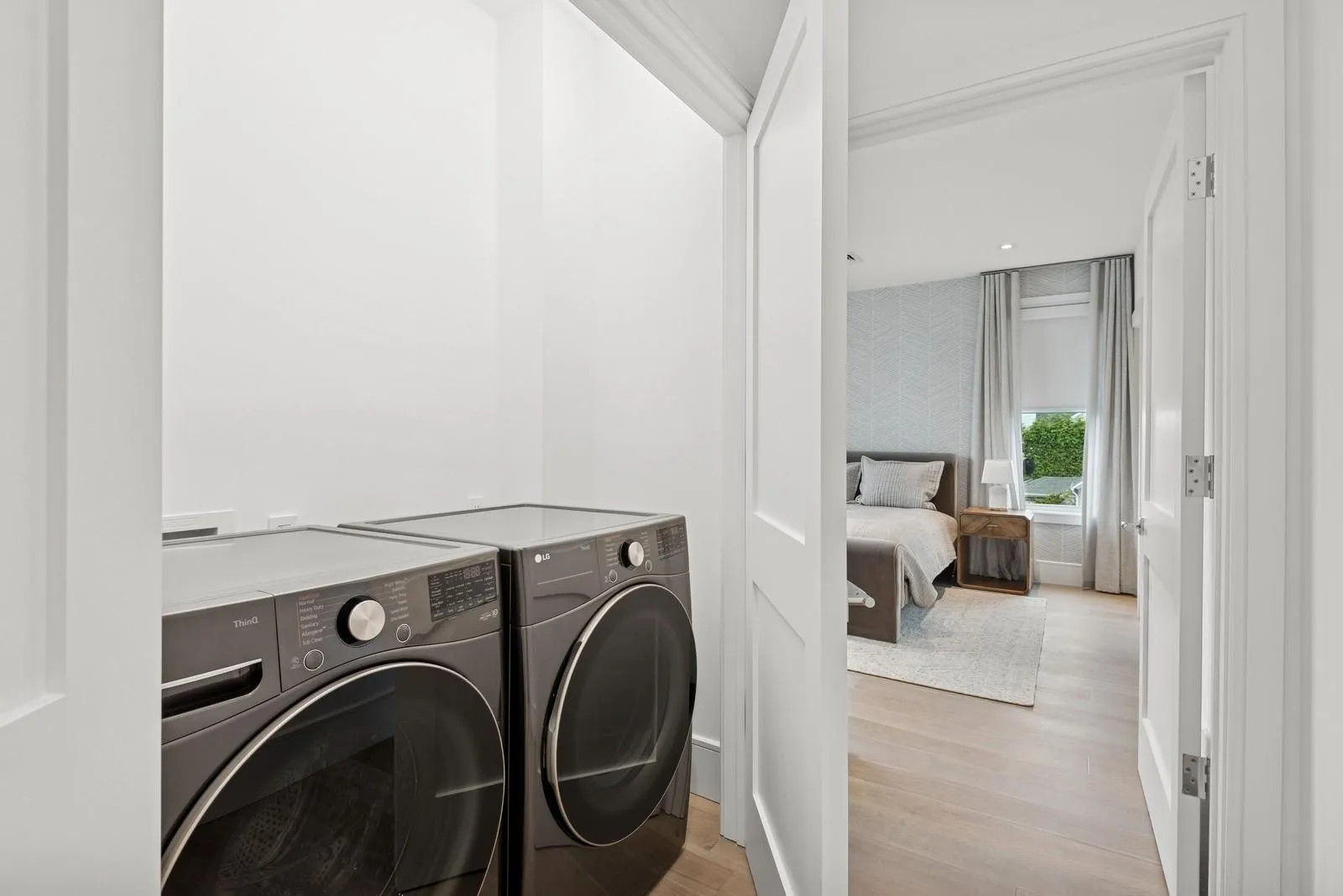 Laundry area featuring washing machine and clothes dryer, light wood-type flooring, and wallpapered walls Laundry area featuring washing machine and clothes dryer, light wood-type flooring, and wallpapered walls