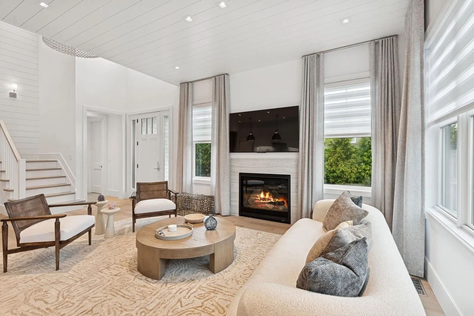 Living room with a glass covered fireplace, wood finished floors, wooden ceiling, stairs, and a towering ceiling Living room with a glass covered fireplace, wood finished floors, wooden ceiling, stairs, and a towering ceiling