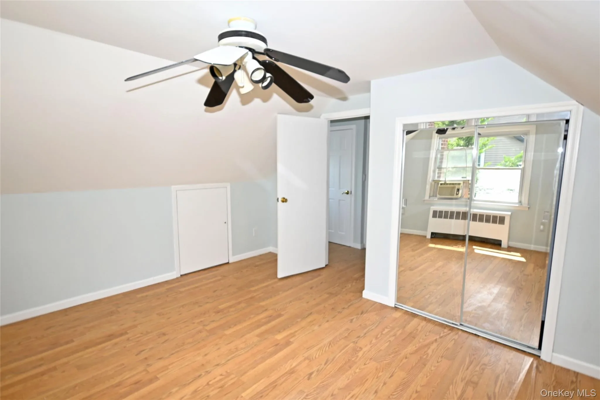 Additional living space with radiator heating unit, light wood finished floors, lofted ceiling, cooling unit, and baseboards Additional living space with radiator heating unit, light wood finished floors, lofted ceiling, cooling unit, and baseboards