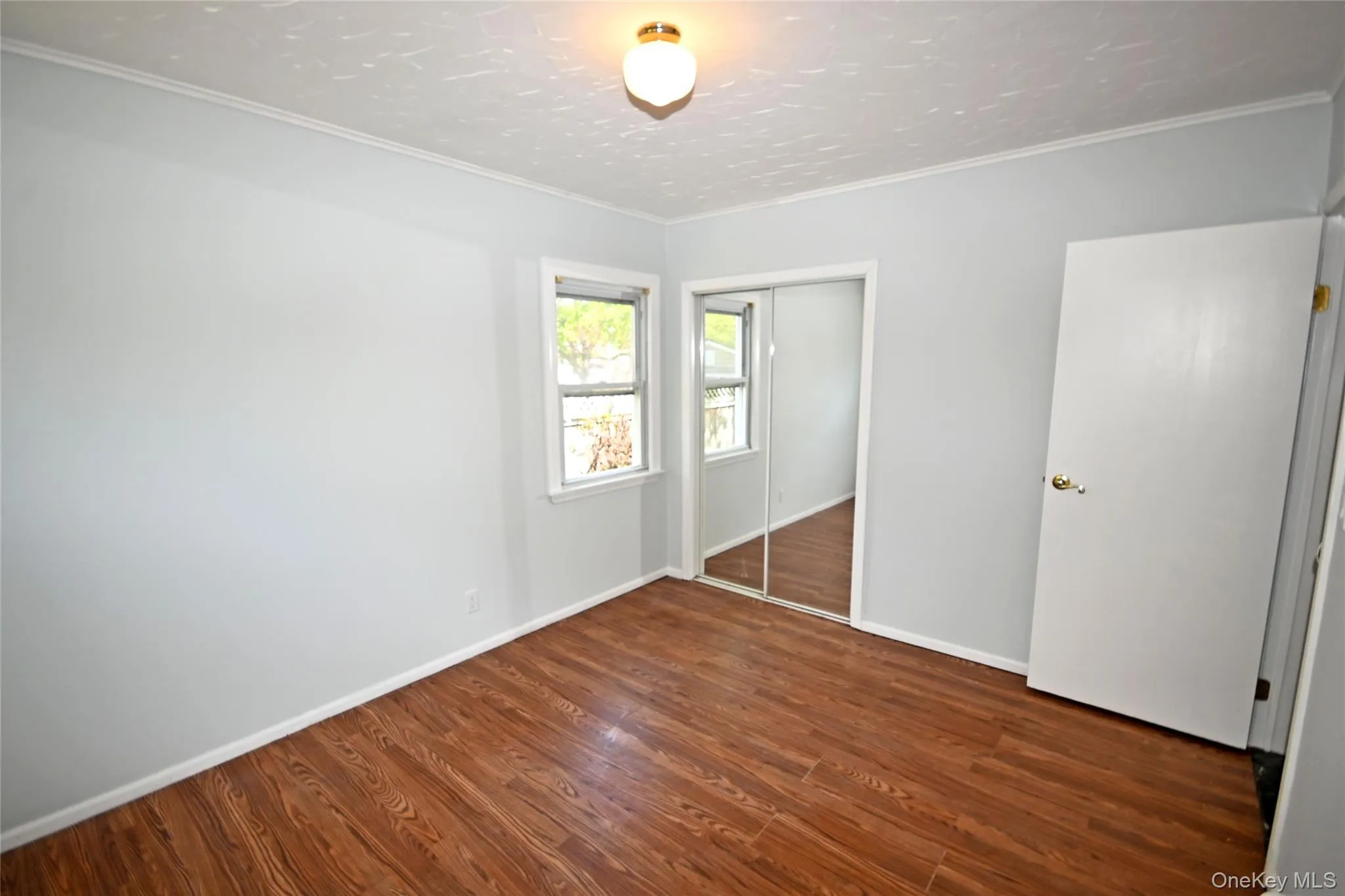 Unfurnished bedroom featuring wood finished floors, a closet, baseboards, and ornamental molding Unfurnished bedroom featuring wood finished floors, a closet, baseboards, and ornamental molding