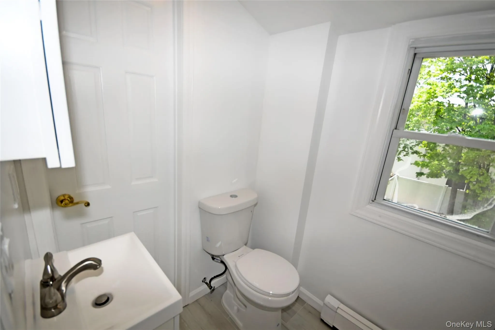 Half bathroom with toilet, wood finished floors, a sink, baseboards, and a baseboard heating unit Half bathroom with toilet, wood finished floors, a sink, baseboards, and a baseboard heating unit