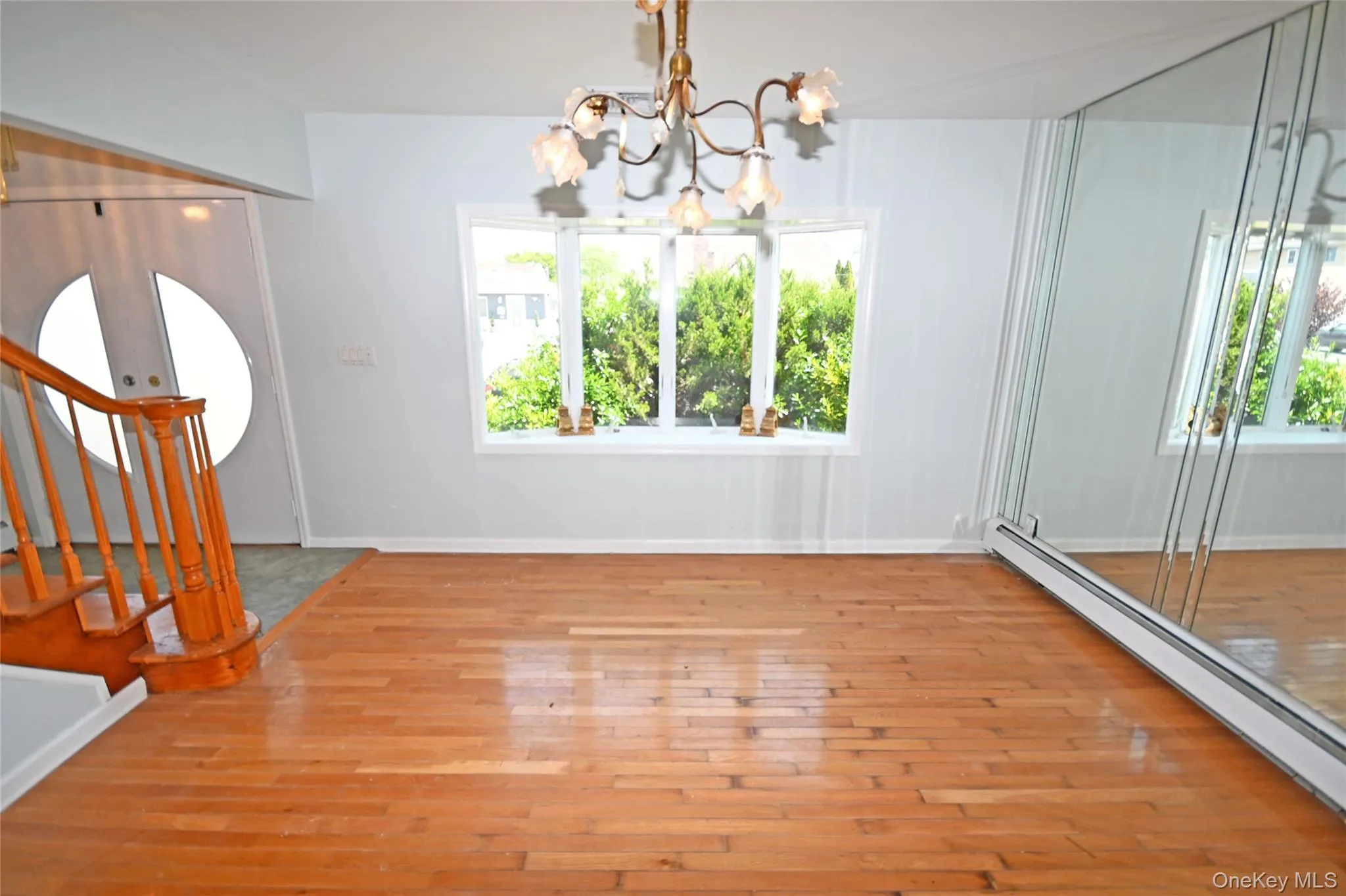 Unfurnished dining area with a baseboard radiator, a chandelier, wood finished floors, and stairs Unfurnished dining area with a baseboard radiator, a chandelier, wood finished floors, and stairs