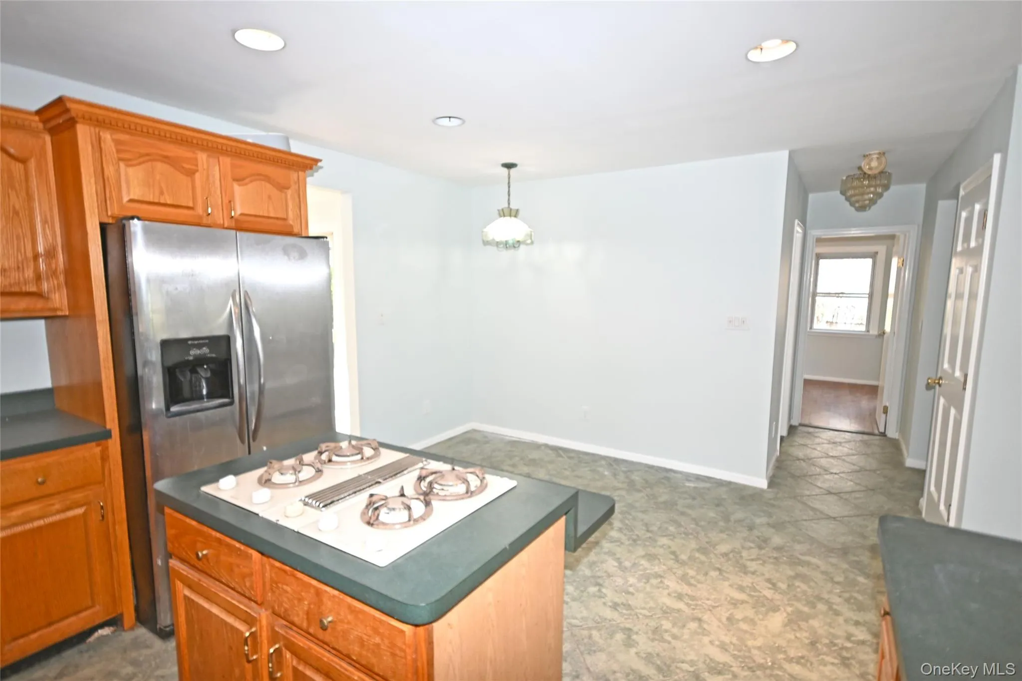 Kitchen featuring stovetop with downdraft, dark countertops, brown cabinetry, a center island, and recessed lighting Kitchen featuring stovetop with downdraft, dark countertops, brown cabinetry, a center island, and recessed lighting