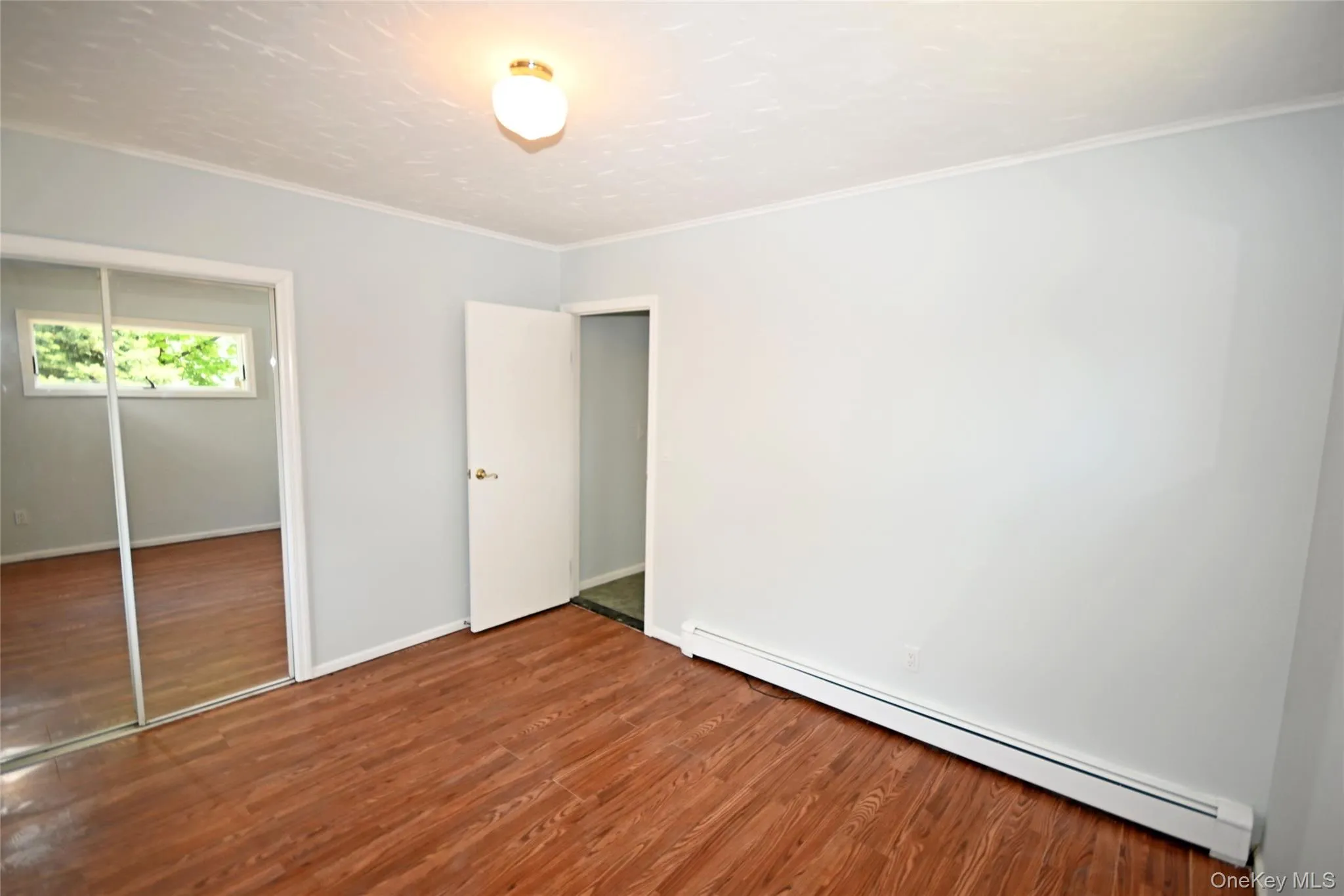 Unfurnished bedroom featuring baseboard heating, wood finished floors, crown molding, a closet, and baseboards Unfurnished bedroom featuring baseboard heating, wood finished floors, crown molding, a closet, and baseboards