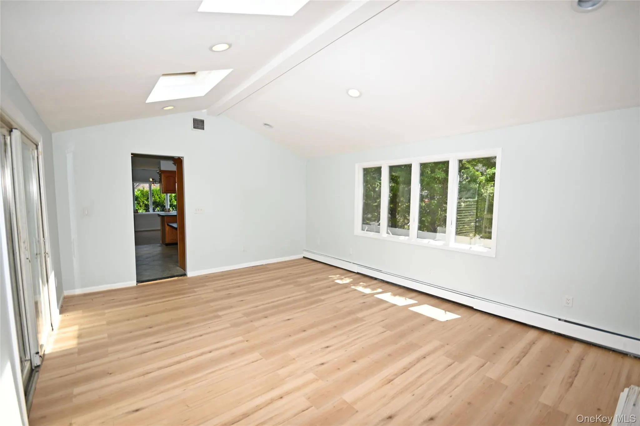 Empty room with a skylight, light wood finished floors, baseboards, recessed lighting, and a baseboard heating unit Empty room with a skylight, light wood finished floors, baseboards, recessed lighting, and a baseboard heating unit