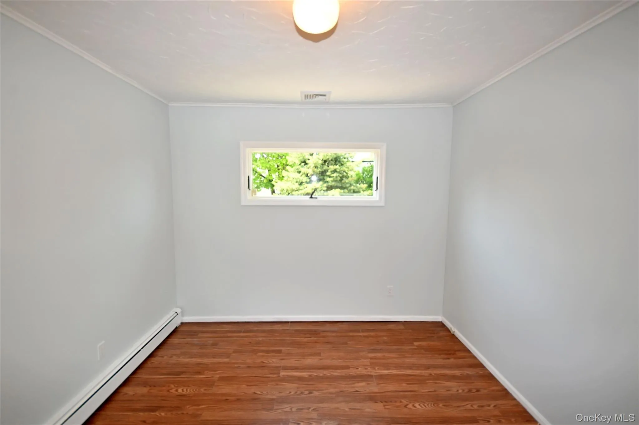 Unfurnished room with a baseboard heating unit, wood finished floors, baseboards, and ornamental molding Unfurnished room with a baseboard heating unit, wood finished floors, baseboards, and ornamental molding