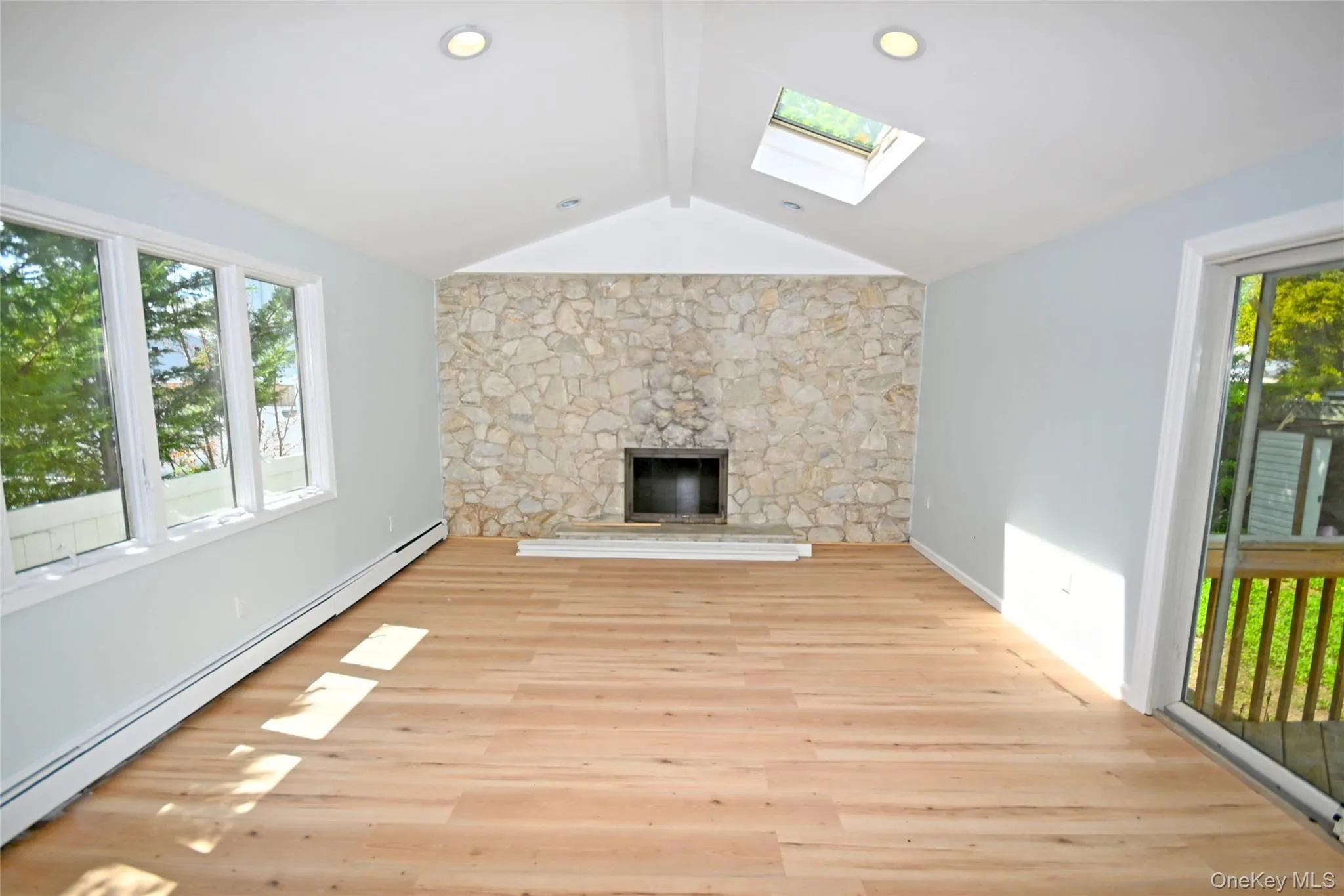 Unfurnished living room with a baseboard radiator, a skylight, a fireplace, and light wood finished floors Unfurnished living room with a baseboard radiator, a skylight, a fireplace, and light wood finished floors