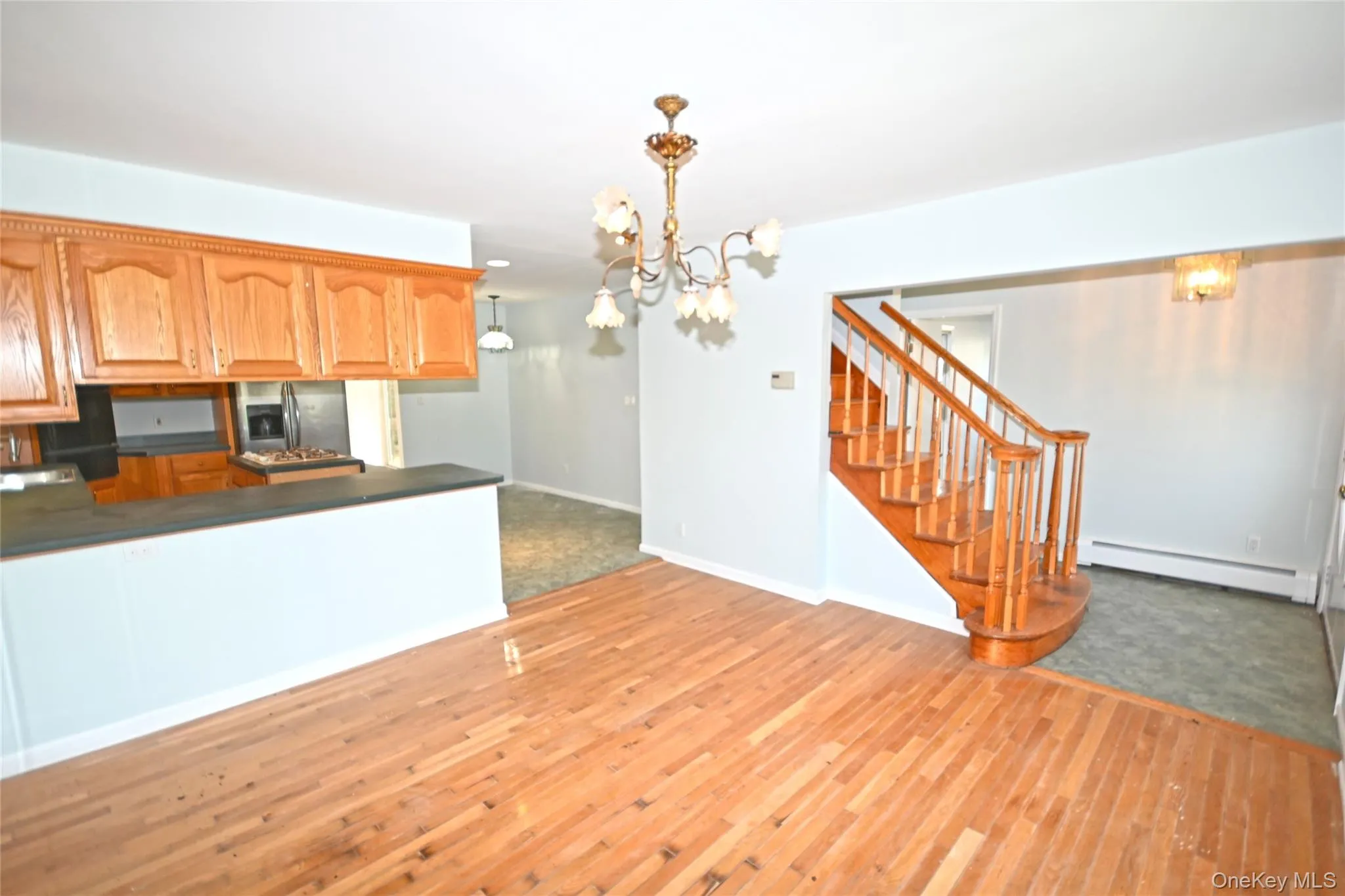 Kitchen featuring a baseboard heating unit, stainless steel fridge with ice dispenser, a chandelier, dark countertops, and light wood-style floors Kitchen featuring a baseboard heating unit, stainless steel fridge with ice dispenser, a chandelier, dark countertops, and light wood-style floors