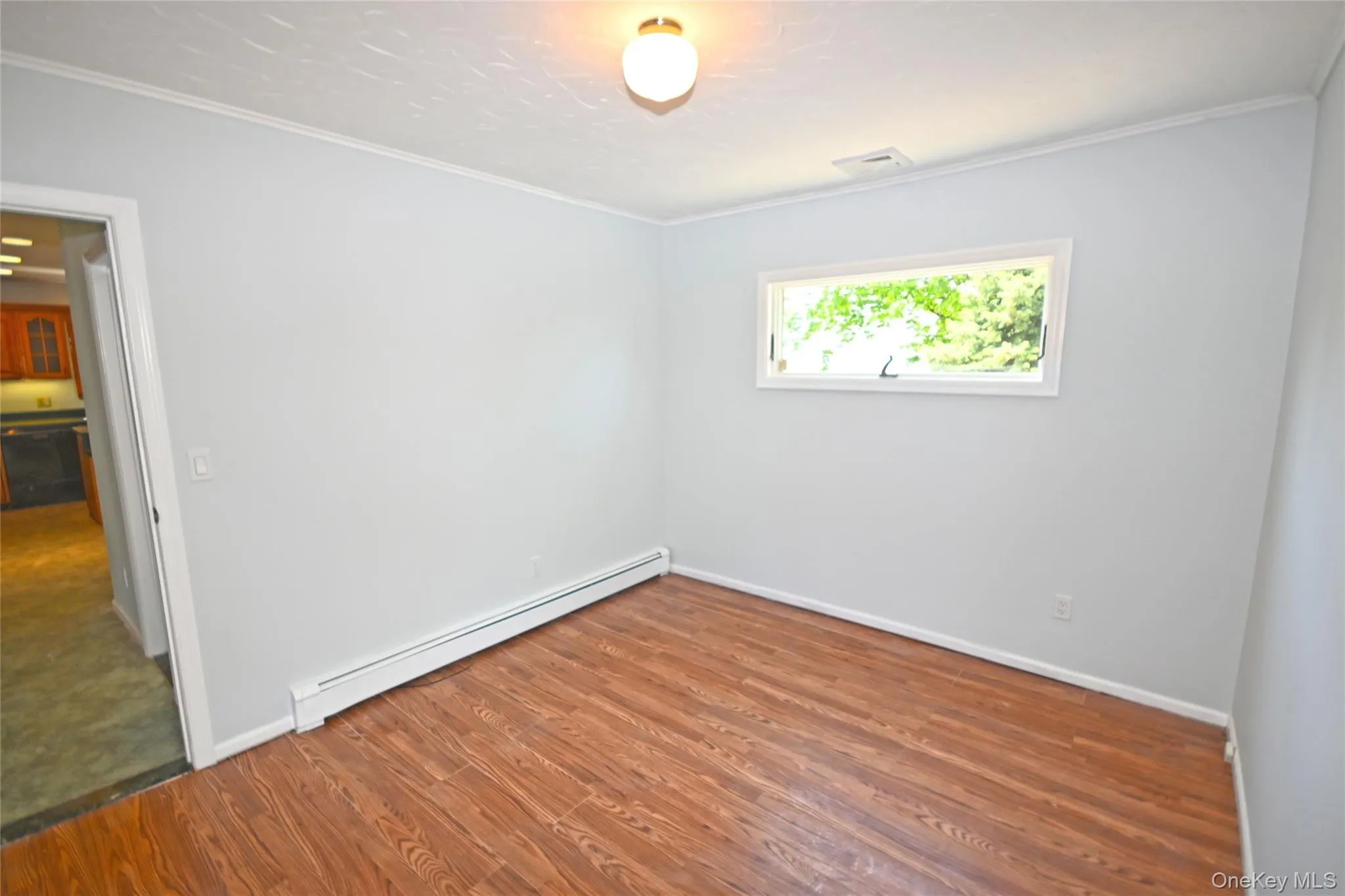 Unfurnished room featuring a baseboard heating unit, wood finished floors, ornamental molding, and baseboards Unfurnished room featuring a baseboard heating unit, wood finished floors, ornamental molding, and baseboards