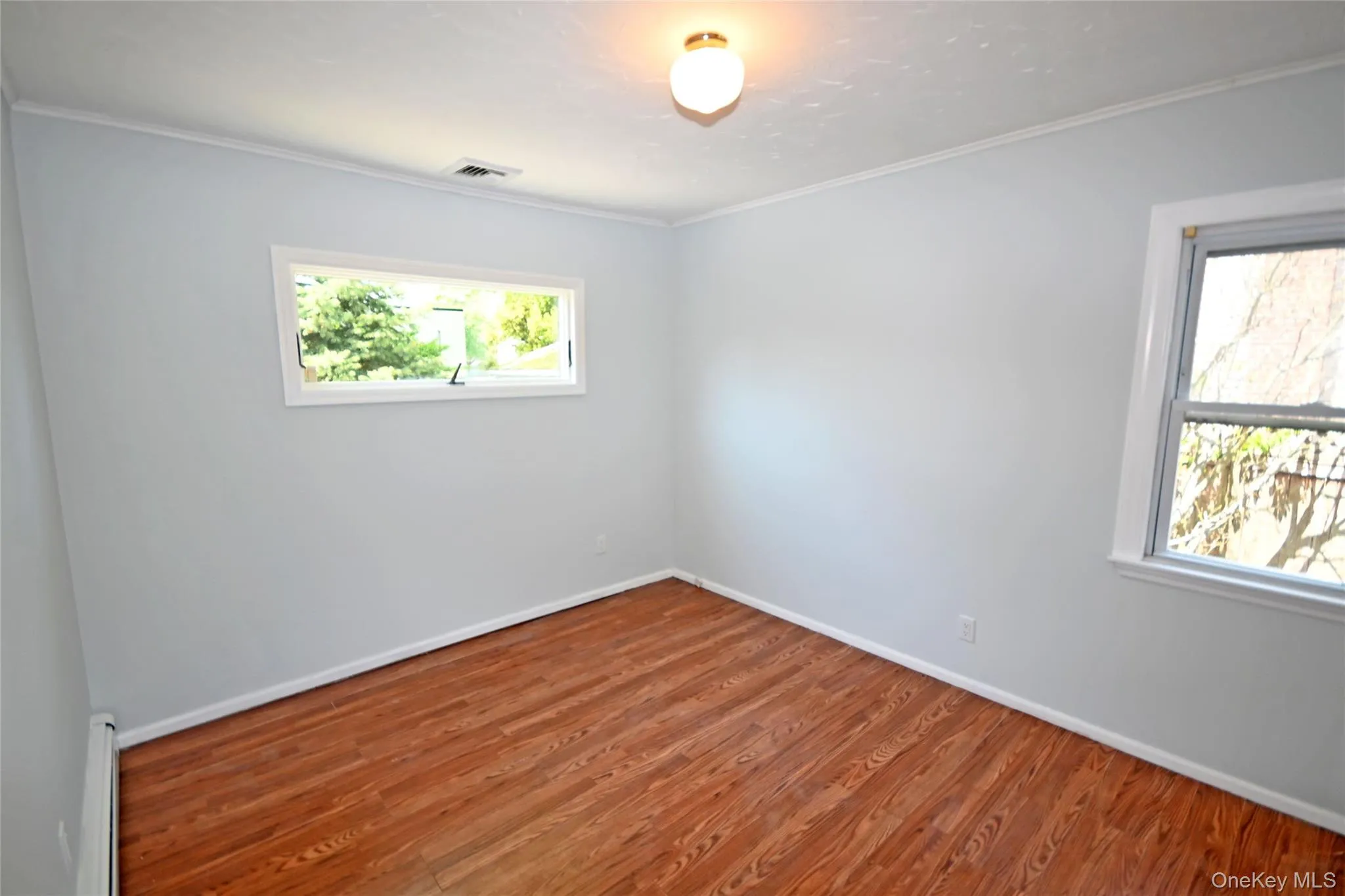 Spare room with a baseboard heating unit, wood finished floors, baseboards, and crown molding Spare room with a baseboard heating unit, wood finished floors, baseboards, and crown molding