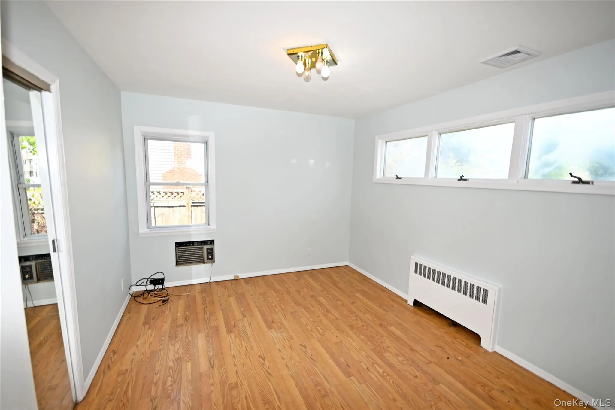 Spare room featuring radiator heating unit, light wood finished floors, and baseboards Spare room featuring radiator heating unit, light wood finished floors, and baseboards