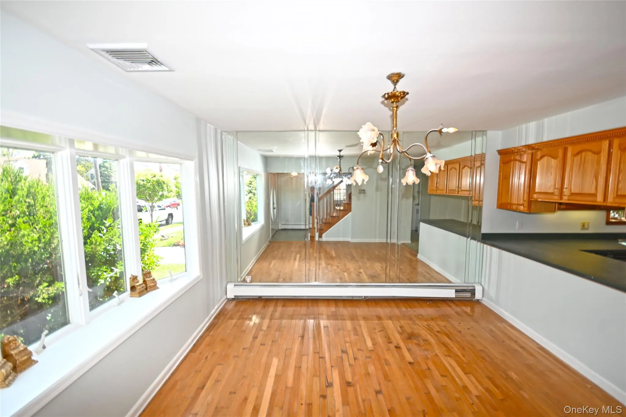 Unfurnished dining area with a baseboard radiator, a chandelier, light wood-style flooring, baseboards, and stairs Unfurnished dining area with a baseboard radiator, a chandelier, light wood-style flooring, baseboards, and stairs