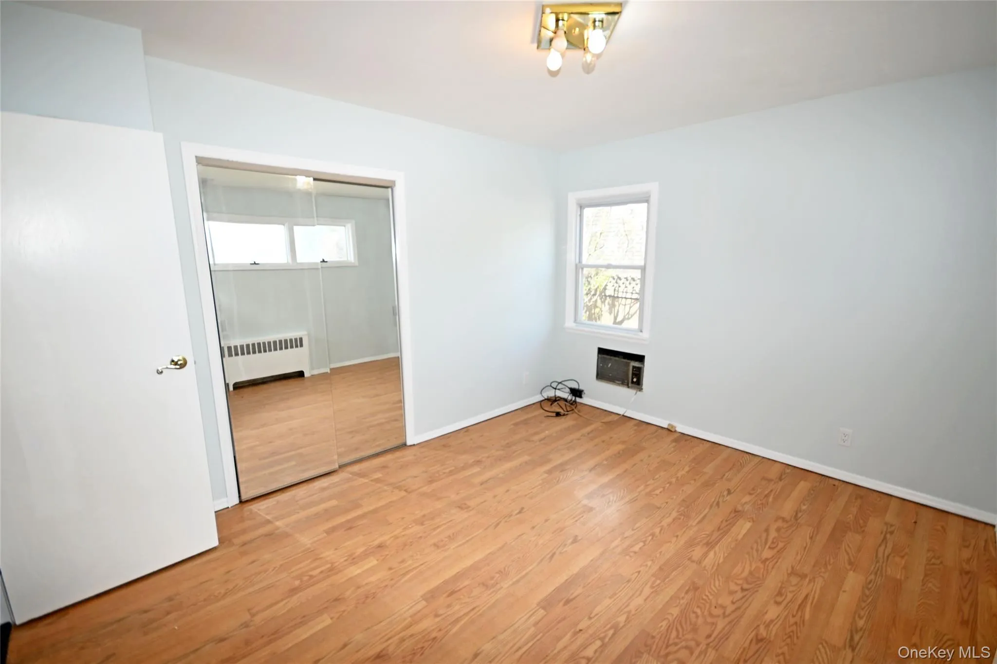 Unfurnished bedroom with radiator heating unit, light wood-type flooring, and baseboards Unfurnished bedroom with radiator heating unit, light wood-type flooring, and baseboards