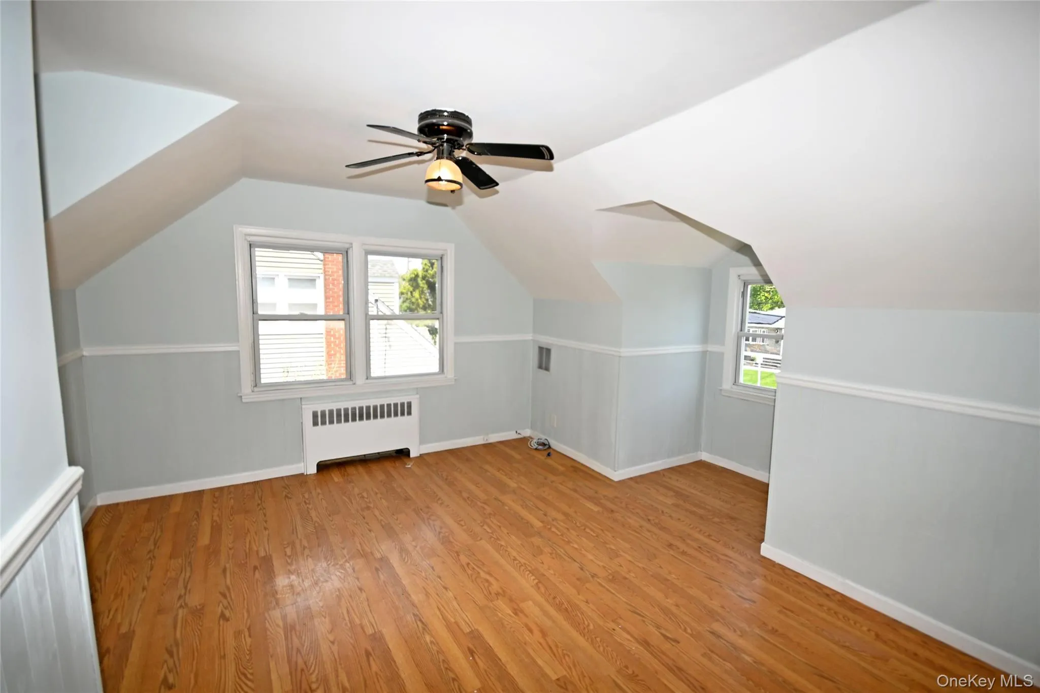 Additional living space featuring radiator, light wood finished floors, baseboards, healthy amount of natural light, and vaulted ceiling Additional living space featuring radiator, light wood finished floors, baseboards, healthy amount of natural light, and vaulted ceiling