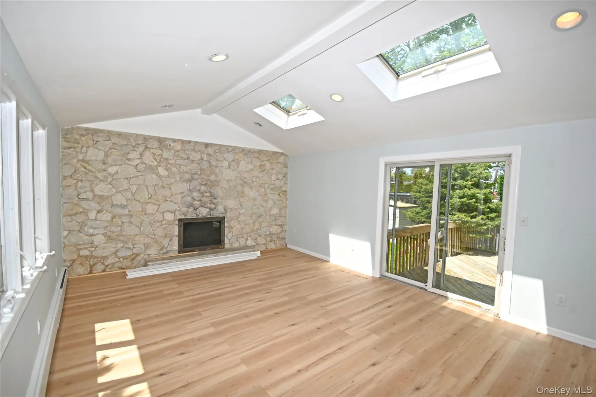 Unfurnished living room featuring a skylight, light wood-style floors, a fireplace, and baseboards Unfurnished living room featuring a skylight, light wood-style floors, a fireplace, and baseboards