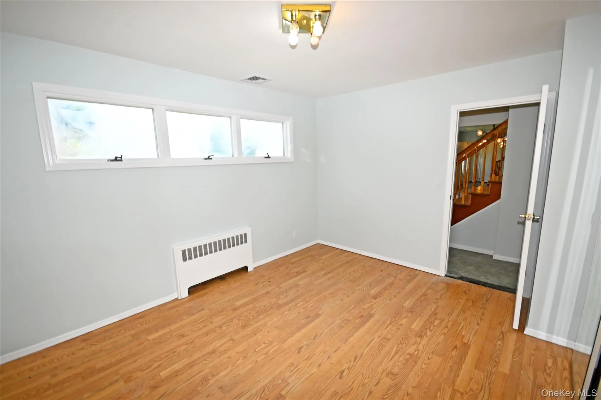 Unfurnished room with radiator, light wood-style flooring, stairs, and baseboards Unfurnished room with radiator, light wood-style flooring, stairs, and baseboards