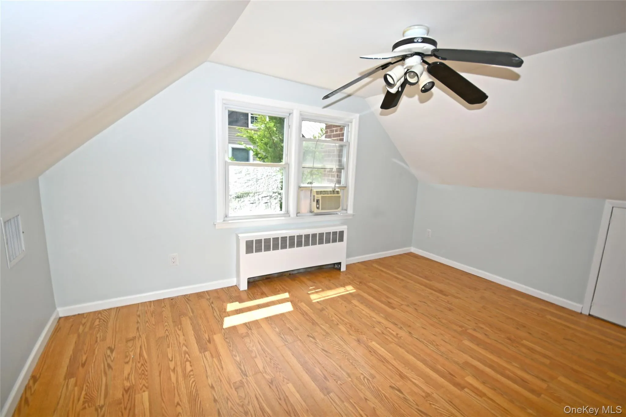 Additional living space featuring radiator heating unit, light wood-style flooring, baseboards, a ceiling fan, and vaulted ceiling Additional living space featuring radiator heating unit, light wood-style flooring, baseboards, a ceiling fan, and vaulted ceiling