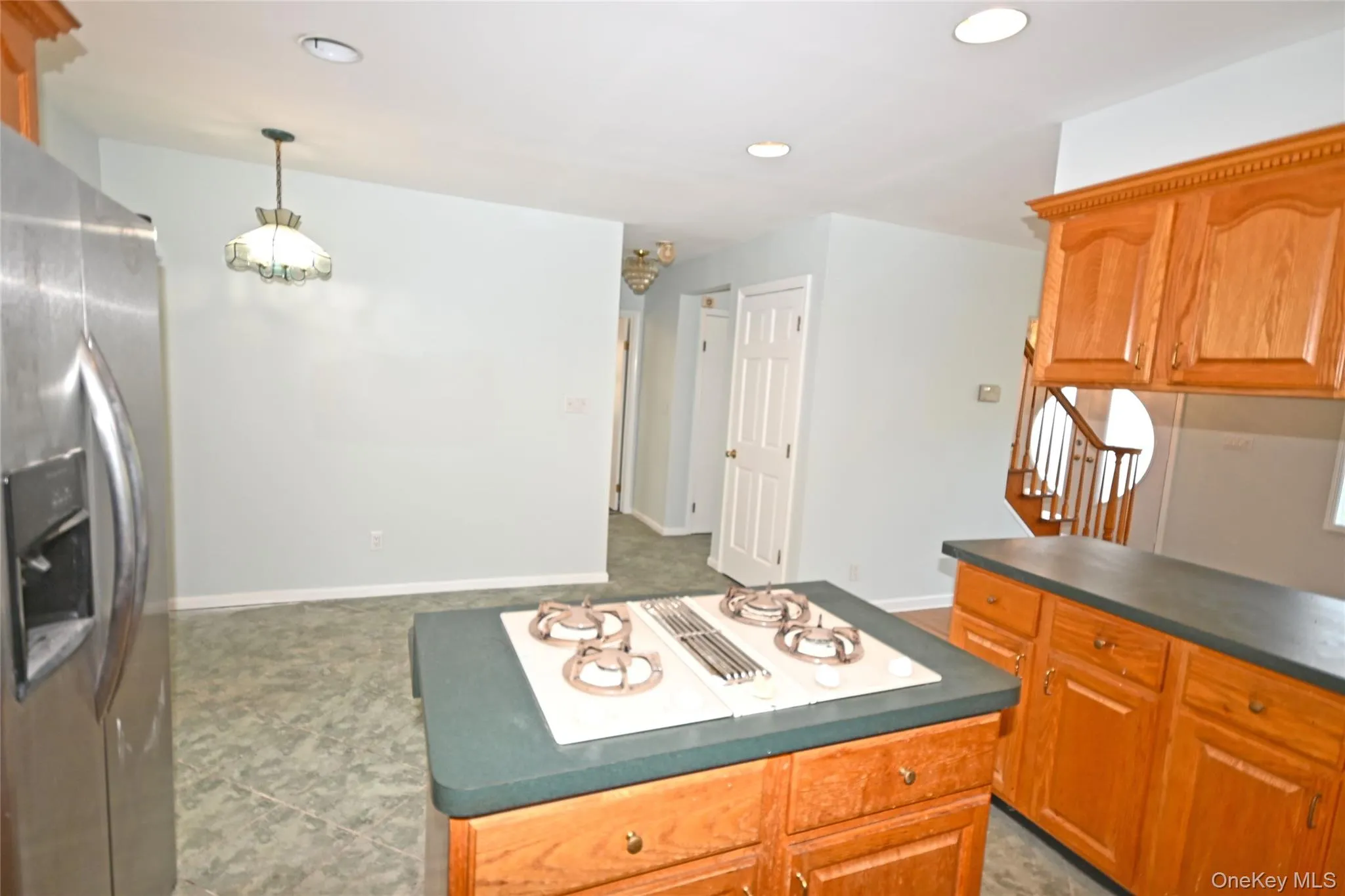 Kitchen featuring stainless steel refrigerator with ice dispenser, dark countertops, recessed lighting, stovetop with downdraft, and pendant lighting Kitchen featuring stainless steel refrigerator with ice dispenser, dark countertops, recessed lighting, stovetop with downdraft, and pendant lighting