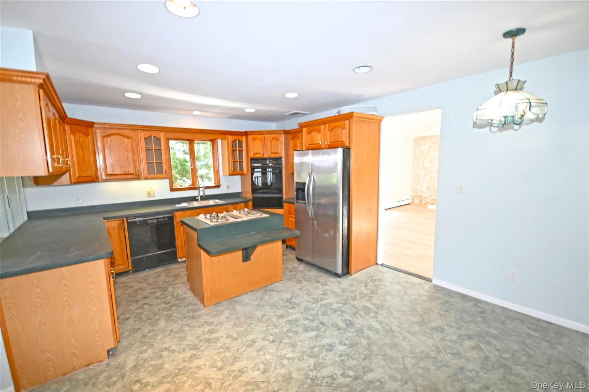 Kitchen featuring stainless steel fridge, black dishwasher, dark countertops, a center island, and glass insert cabinets Kitchen featuring stainless steel fridge, black dishwasher, dark countertops, a center island, and glass insert cabinets