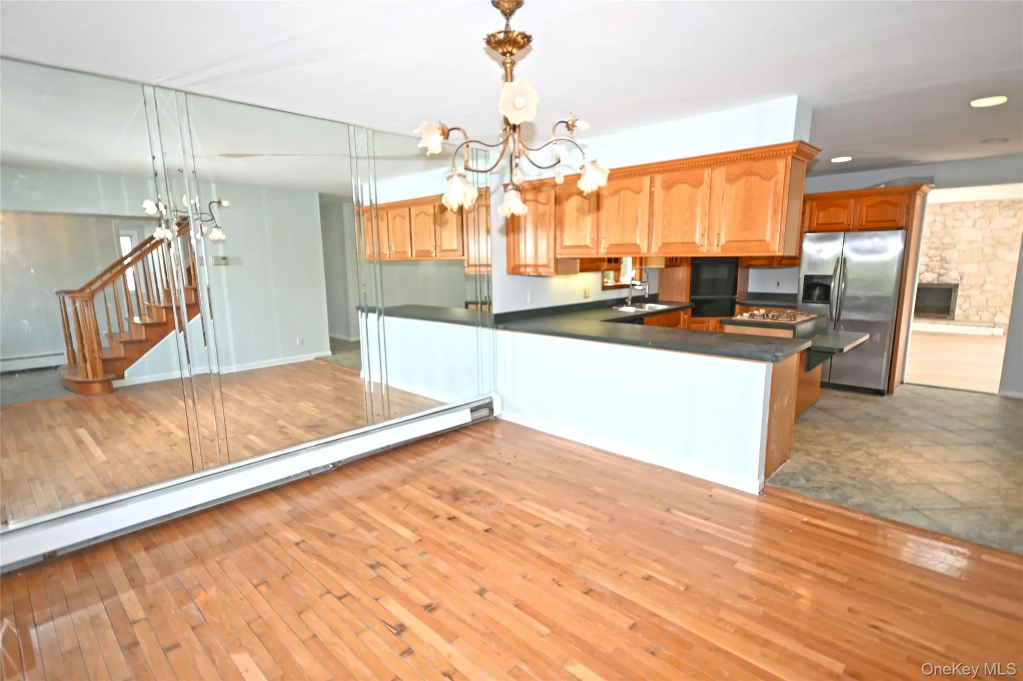 Kitchen featuring stainless steel fridge with ice dispenser, a chandelier, dark countertops, a sink, and light wood-style flooring Kitchen featuring stainless steel fridge with ice dispenser, a chandelier, dark countertops, a sink, and light wood-style flooring