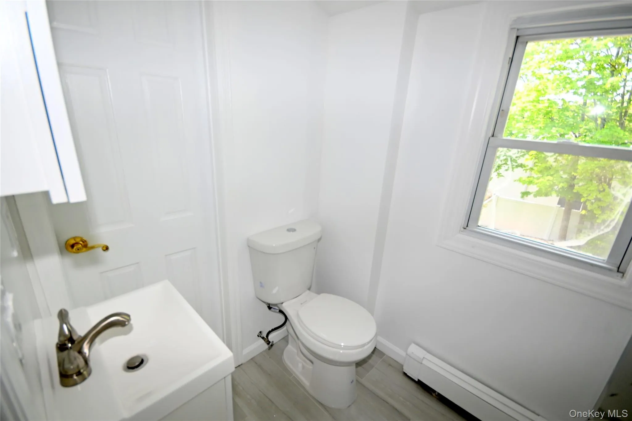 Bathroom featuring a baseboard heating unit, toilet, plenty of natural light, and wood finished floors Bathroom featuring a baseboard heating unit, toilet, plenty of natural light, and wood finished floors