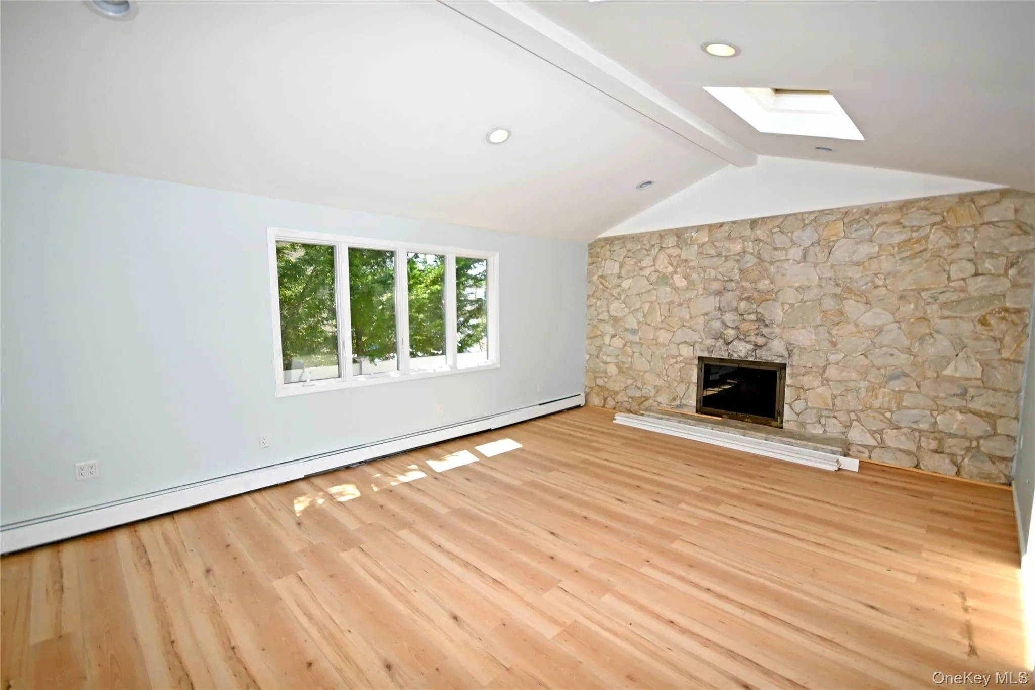 Unfurnished living room featuring a skylight, baseboard heating, wood finished floors, and a fireplace Unfurnished living room featuring a skylight, baseboard heating, wood finished floors, and a fireplace
