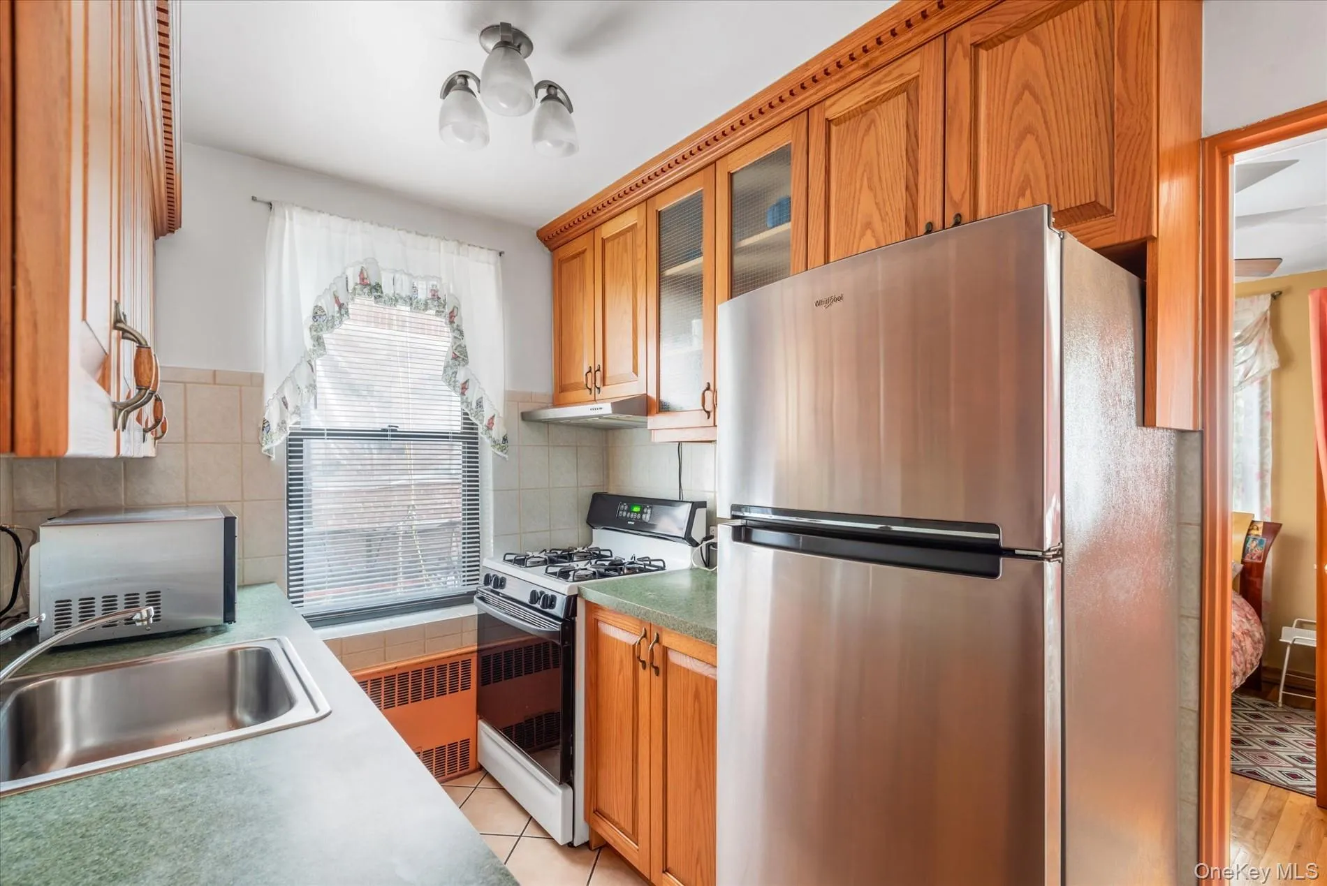 Kitchen with freestanding refrigerator, white range with gas stovetop, under cabinet range hood, radiator heating unit, and a sink Kitchen with freestanding refrigerator, white range with gas stovetop, under cabinet range hood, radiator heating unit, and a sink