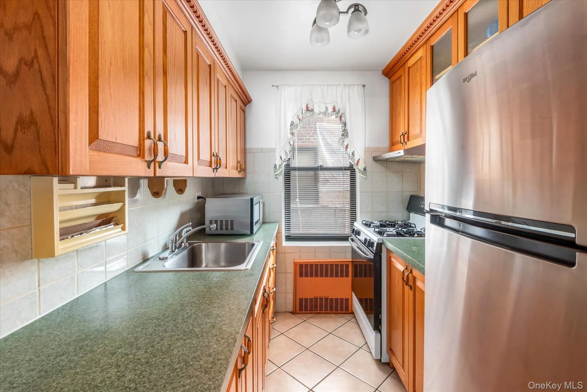 Kitchen featuring appliances with stainless steel finishes, radiator, a sink, under cabinet range hood, and brown cabinets Kitchen featuring appliances with stainless steel finishes, radiator, a sink, under cabinet range hood, and brown cabinets