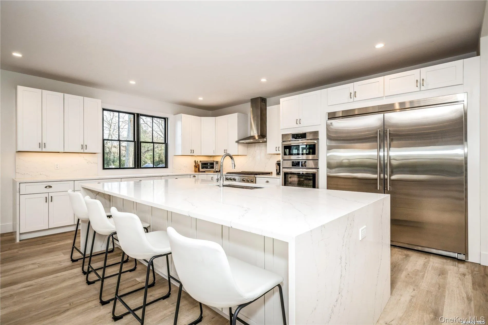 Kitchen with stainless steel appliances, wall chimney range hood, light wood-type flooring, light stone countertops, and recessed lighting Kitchen with stainless steel appliances, wall chimney range hood, light wood-type flooring, light stone countertops, and recessed lighting