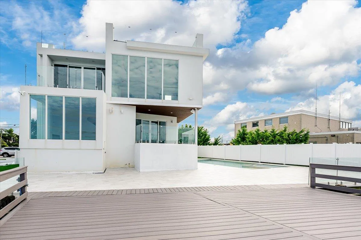 Rear view of house featuring stucco siding, fence, a wooden deck, a swimming pool, and a sunroom Rear view of house featuring stucco siding, fence, a wooden deck, a swimming pool, and a sunroom