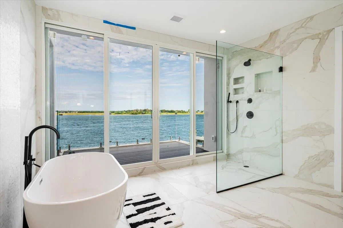 Full bathroom with a freestanding bath, a marble finish shower, a water view, and marble tiled floors Full bathroom with a freestanding bath, a marble finish shower, a water view, and marble tiled floors